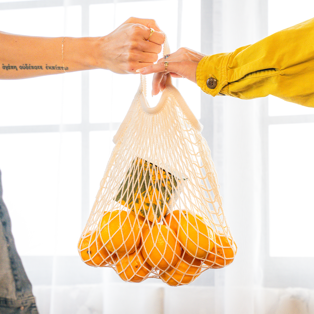 Person handing over bag of fresh lemons and Hye Harvest Meyer Lemon THC Gummies to another person against a white background.