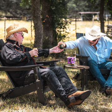 Two men in cowboy hats enjoy Hye Harvest Texas hemp products outdoors on a farm in Hye, Texas.