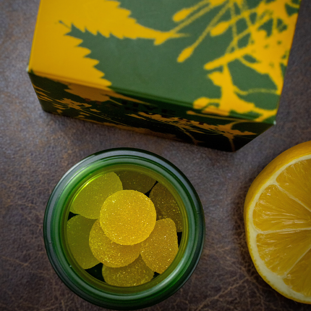 Jar of bright, yellow Meyer Lemon THC Gummies in a green and yellow box in the background